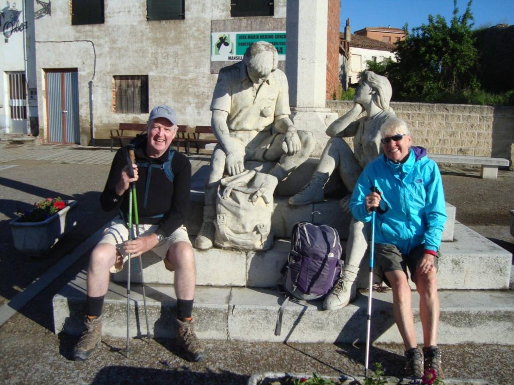 2 pilgrims on the Camino de Santiago pose by statues