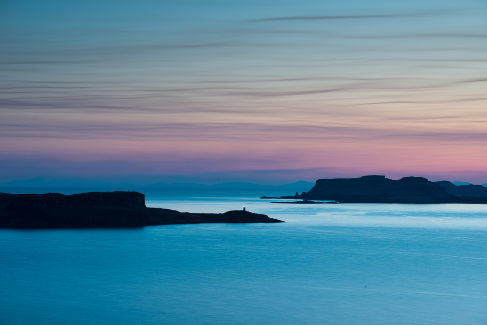 Oronsay island sits in a blue sea with the sunrise tinting the skies