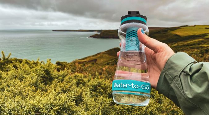 person holding a Water-To-Go water bottle with scenic background